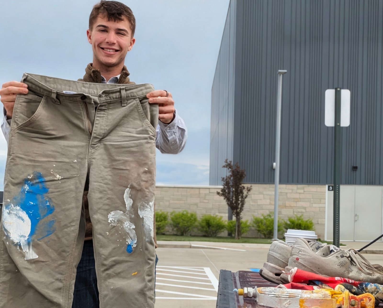 Karter Otte holding up paint-stained work pants next to his truck bed