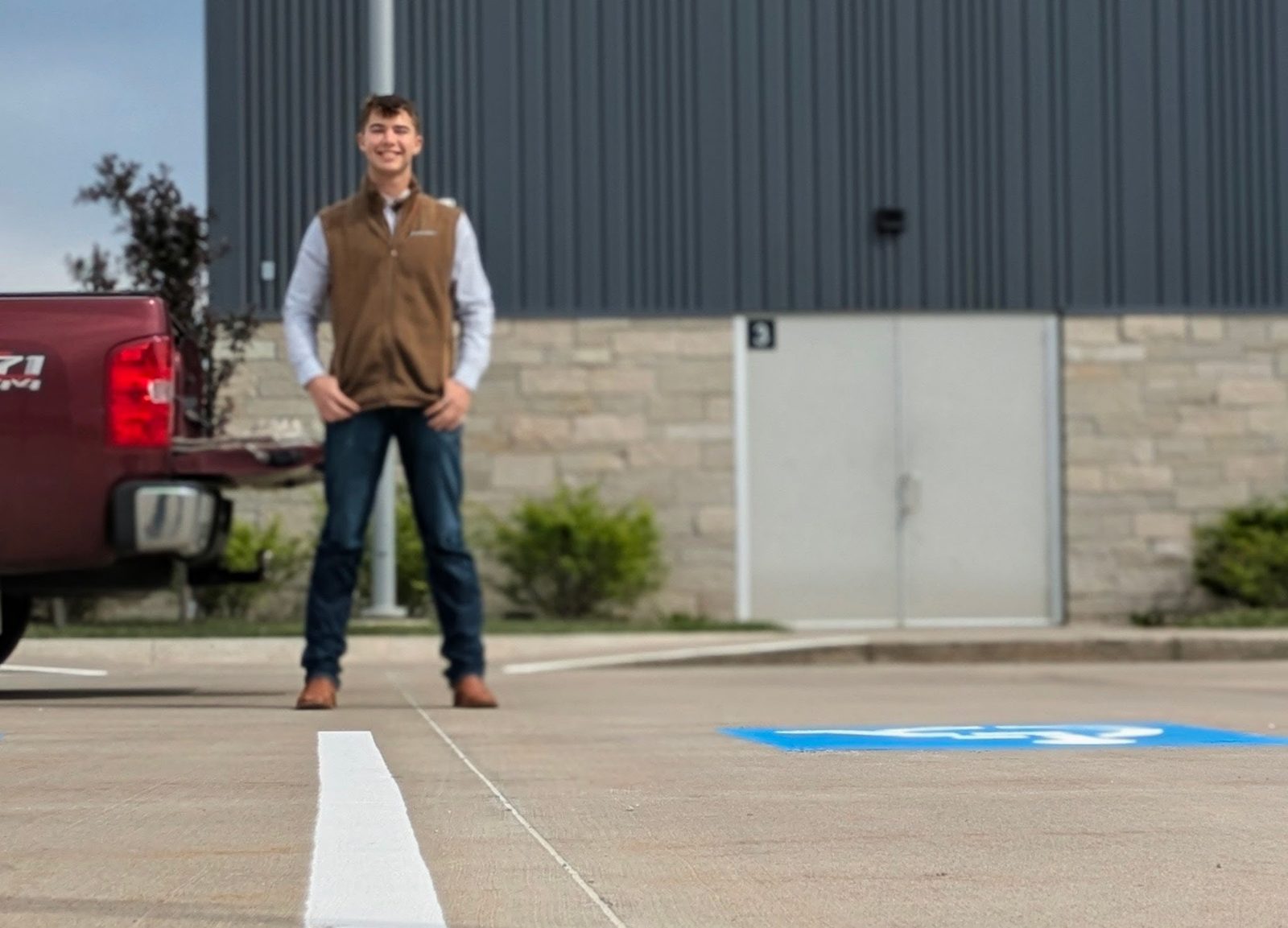 Karter Otte standing in a freshly striped parking lot beside a new white stall line and blue ADA symbol